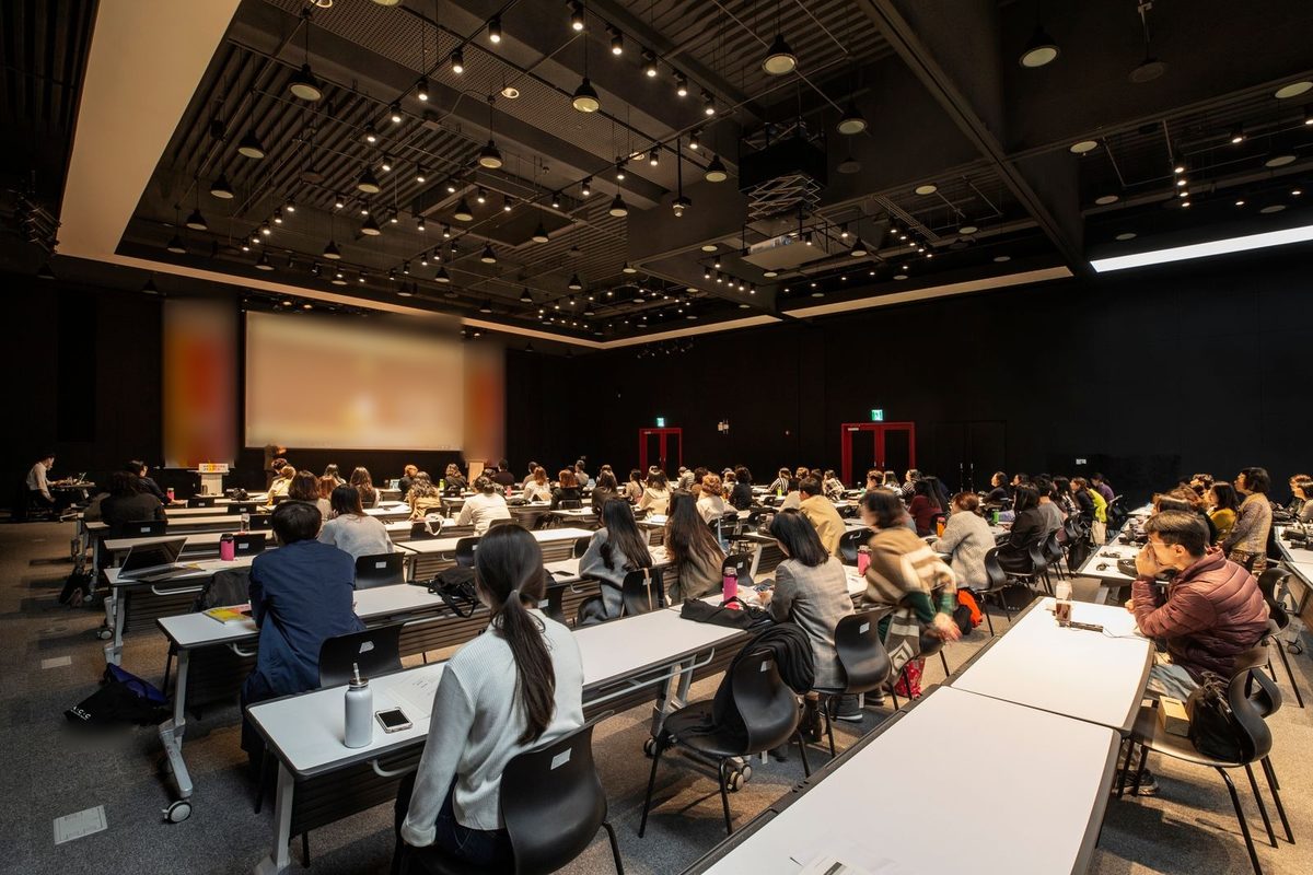 広い会場で、参加者が正面のスクリーンと登壇者を見ているセミナー
