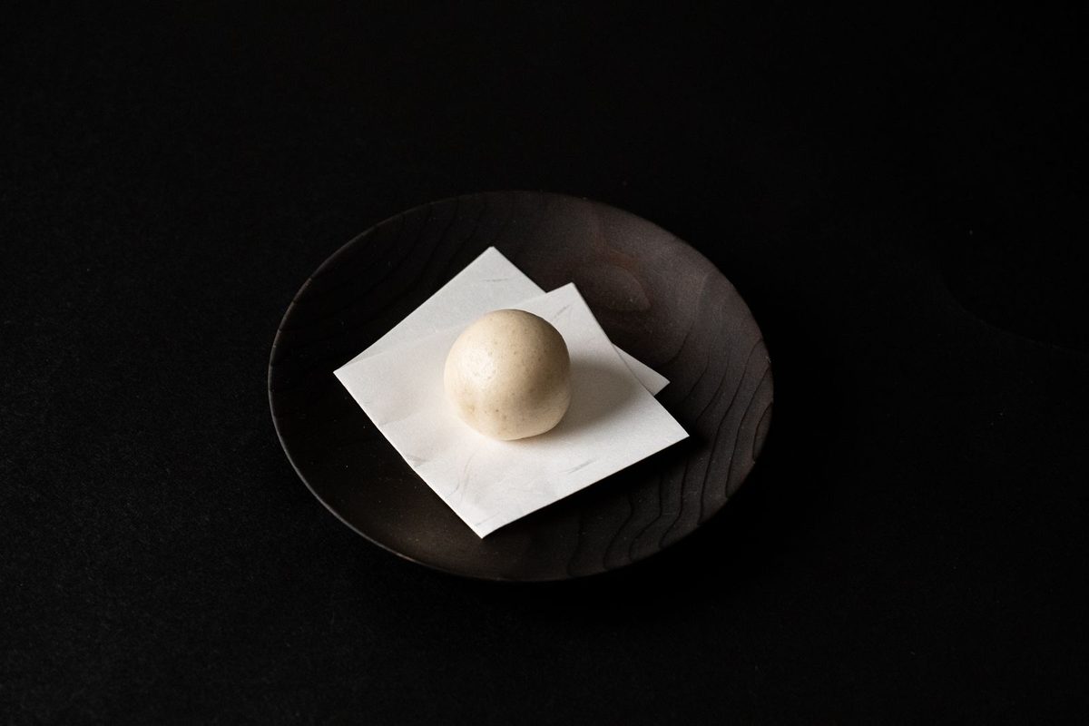 暗い背景で、漆の皿にのった和菓子にひとつの光が当たっている